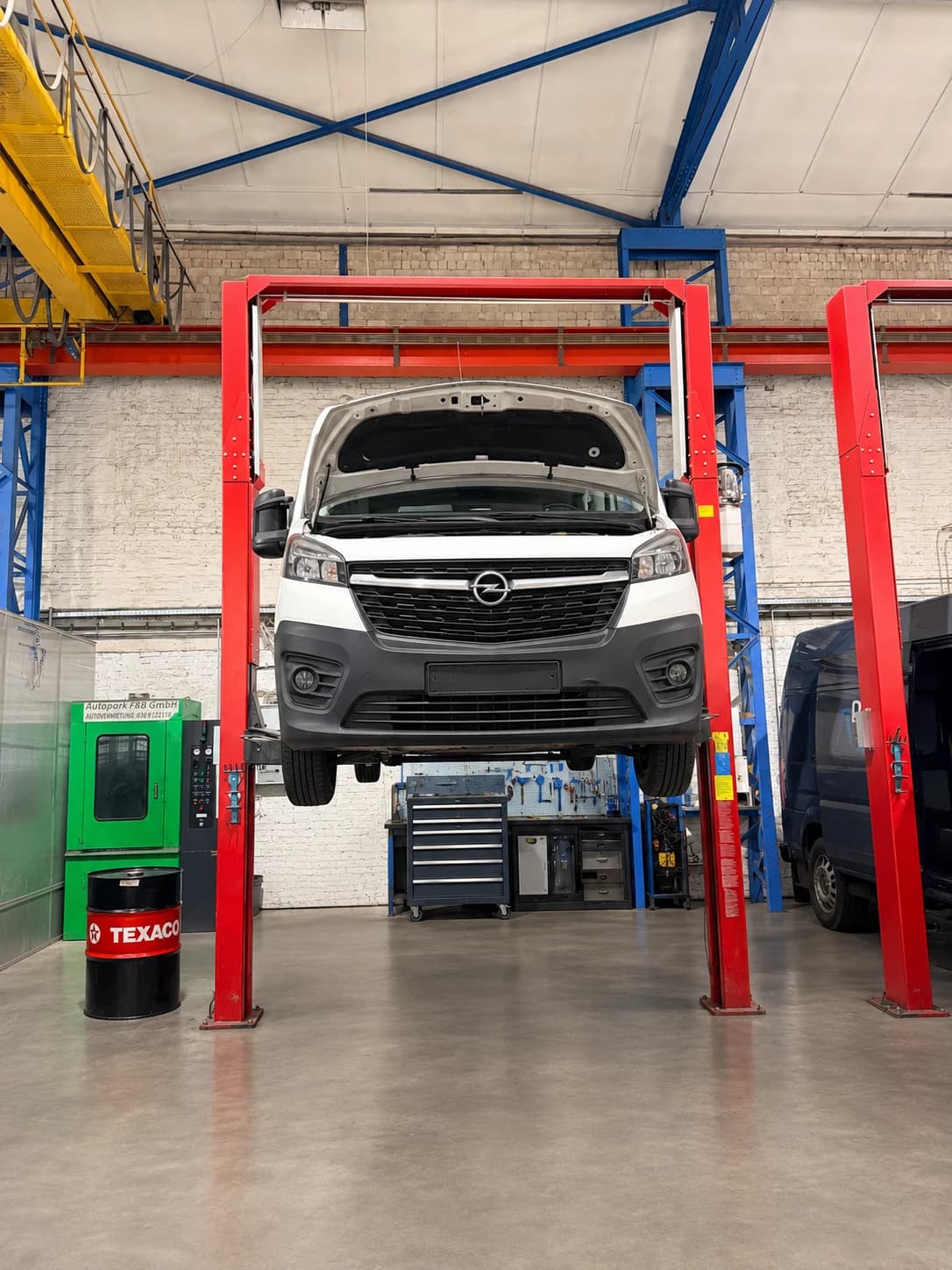 Transporter mit geöffneter Motorhaube auf einer roten Hebebühne